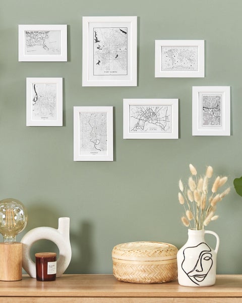 Wanddekoration mit mehreren gerahmten Stadtplänen, dekorativer Lampe, Kerze und Trockenblumen auf einem Regal