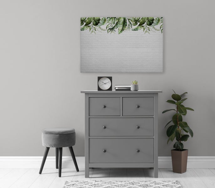 Wandbild mit Blattmotiv auf einer Backsteinwand über einer grauen Kommode mit Hocker und Zimmerpflanze in einem modern eingerichteten Raum