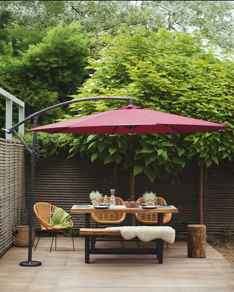 Ampelschirm mit roter Bespannung, dunklem Metallgestell und Kreuzfußständer.