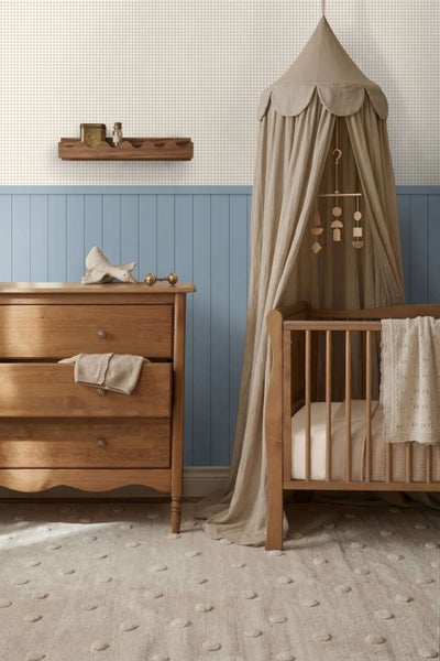 Einrichtung eines Kinderzimmers mit Holzkommode, Gitterbett mit Betthimmel, Wandregal und getäfelter Wandgestaltung.