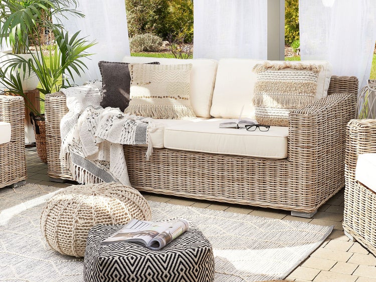 Gartenszene mit Rattansofa, Kissen, Decke, Poufs und Teppich