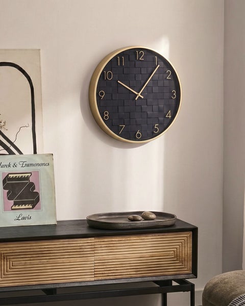 Moderne Wanduhr mit rundem Gehäuse und Ziffernblatt in Kacheloptik über einer Anrichte mit Dekorationsartikeln