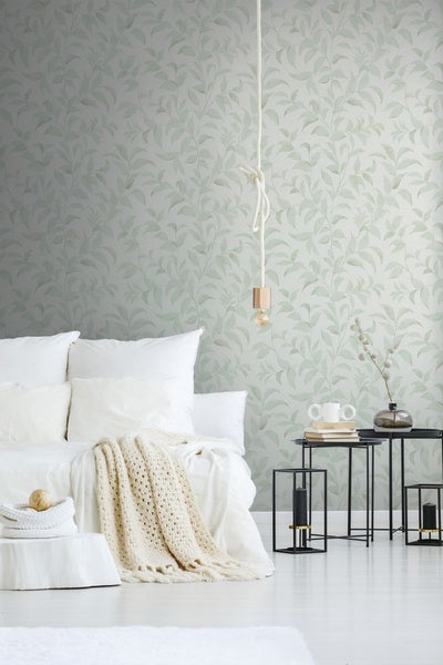 Helles Schlafzimmer mit Bett, Beistelltischen und Wandtapete mit Pflanzenmuster.