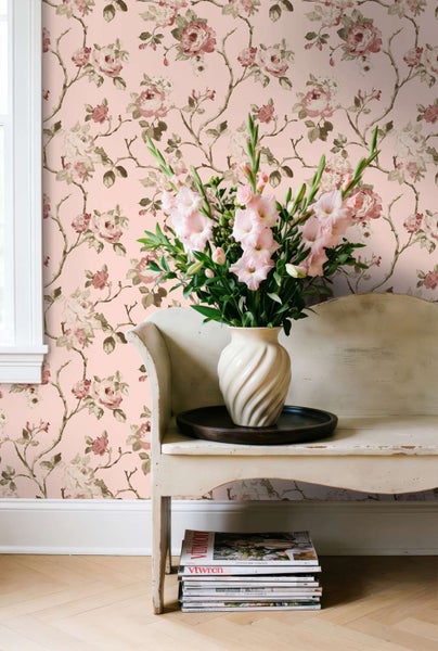 Vliestapete mit romantischem Rosenmuster vor einem hellen Möbelstück mit Blumenstrauß in einer Vase