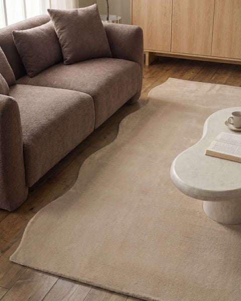 Moderner Teppich mit unregelmäßiger, organischer Form auf Holzboden neben einem braunen Sofa und einem weißen Couchtisch.