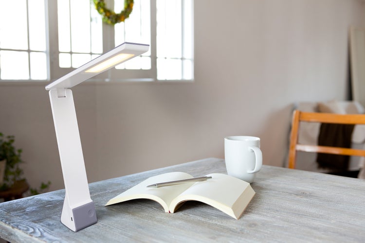 Schreibtischszene mit LED-Lampe, Notizbuch, Stift und Tasse auf einem Tisch