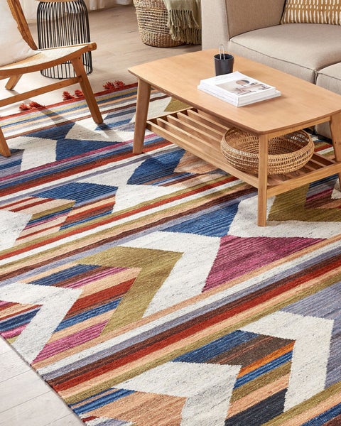 Mehrfarbiger Teppich mit geometrischem Zickzack-Muster in einem hellen, modernen Wohnzimmer mit Holz-Couchtisch und Sofa.