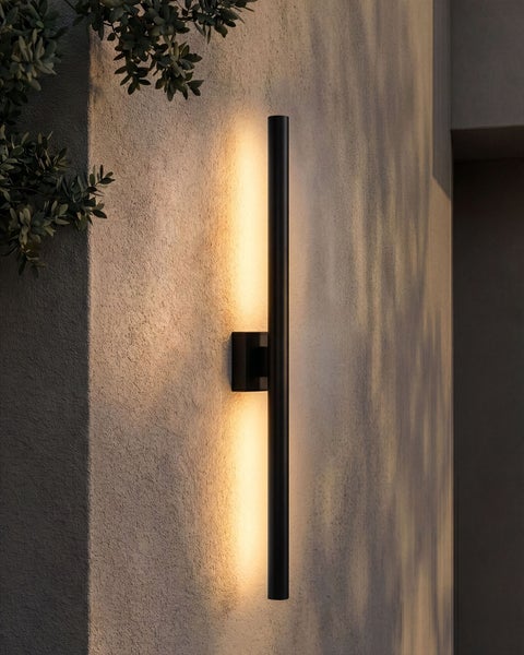 Schlanke, schwarze LED-Außenwandleuchte in Röhrenform mit warmweißem, indirektem Lichtschein nach oben und unten an einer verputzten Wand.