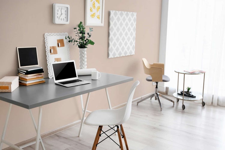 Modernes Arbeitszimmer mit grauem Schreibtisch, weißen Tischböcken, Laptop, weißem Schalenstuhl und hellen Holzböden in organisierter Atmosphäre.