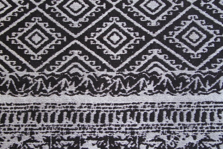 Detailaufnahme eines gewebten Teppichs mit geometrischem Ethno-Muster in Schwarz und Weiß.