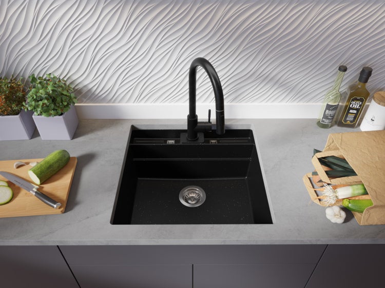 Schwarze Küchenspüle mit Armatur, Gemüse, Ölflaschen und Kräutern auf der Arbeitsplatte.