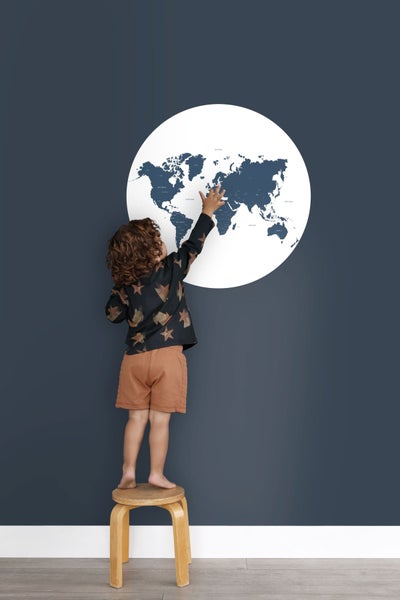 Junge steht auf einem Hocker und berührt eine Weltkarte an der Wand.