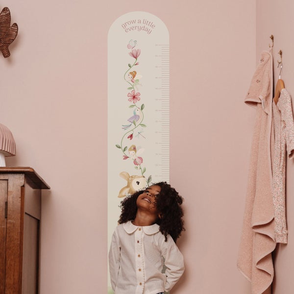 Wandsticker Messlatte für Kinder mit Tiermotiven und Feen, angebracht an einer Wand im Kinderzimmer, neben einem Kind stehend.