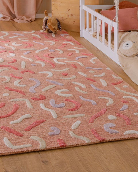 Kinderteppich mit abstraktem Wellenmuster in einem hellen Kinderzimmer neben einem weißen Kinderbett auf Holzboden.