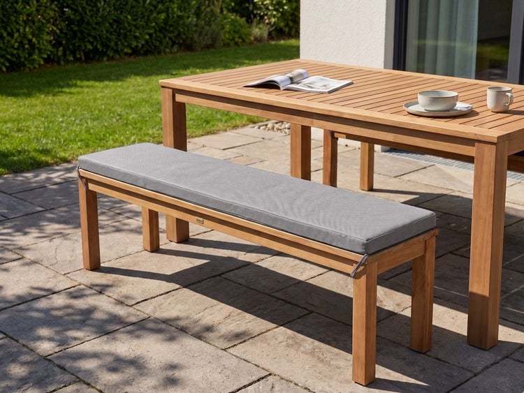 Gartenbank aus Holz mit einem rechteckigen Sitzkissen auf einer Steinterrasse neben einem Gartentisch.