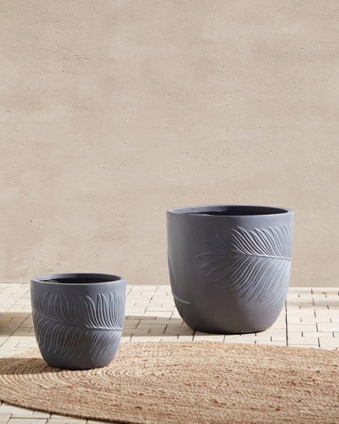 Zwei graue Pflanzgefäße mit Blattmuster auf einer Terrasse.