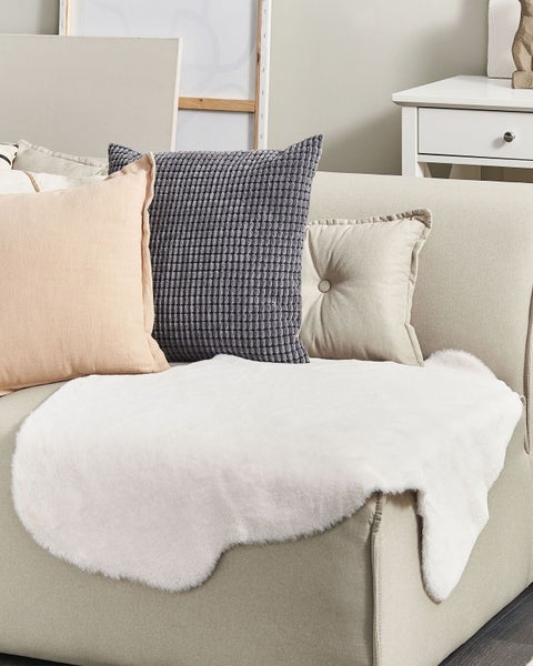 Dekoratives Arrangement mit Kissen und Schaffell auf einem Sofa