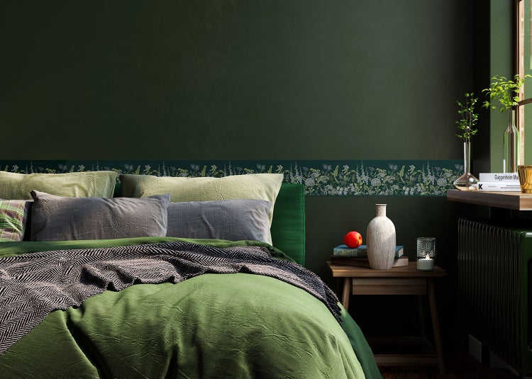 Dunkelgrünes Schlafzimmer mit floraler Tapetenbordüre, Bett mit grünen Textilien und hölzernem Nachttisch.