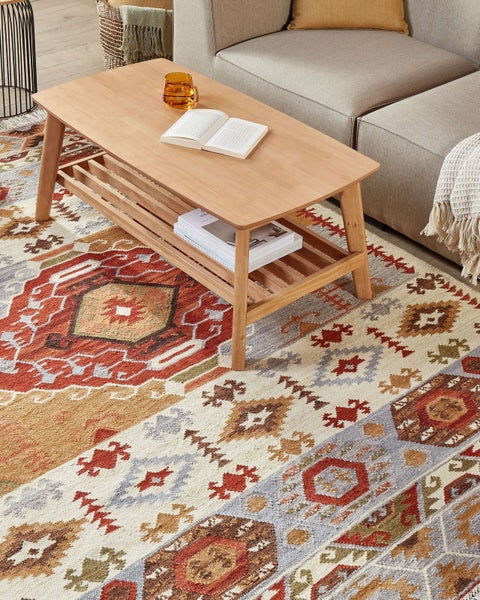 Szene mit einem Wohnzimmerteppich mit geometrischen Mustern unter einem Holztisch neben einem Sofa.