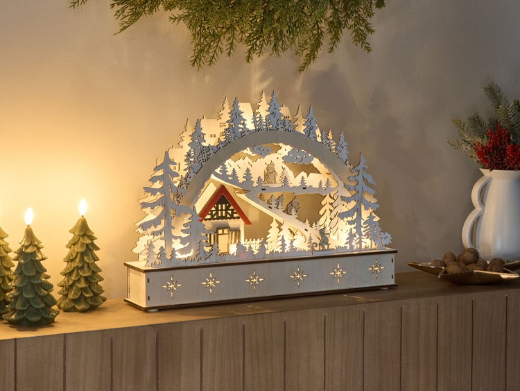Dekorative Fensterleuchte mit Winterlandschaft und Baumkerzen auf einer Kommode