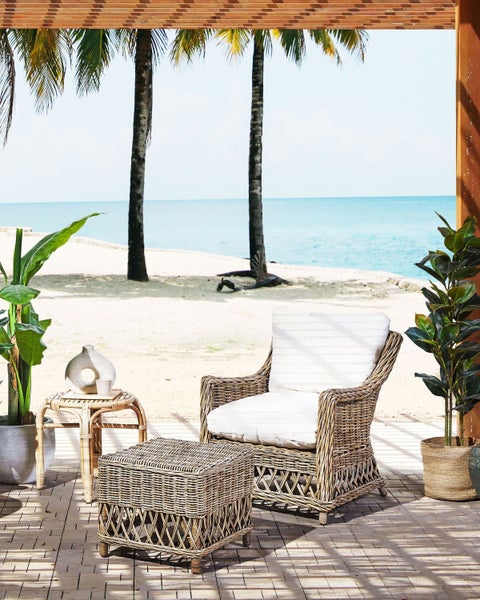 Szene im Freien mit Rattansessel, Hocker und Beistelltisch auf einer Terrasse mit Blick auf den Strand