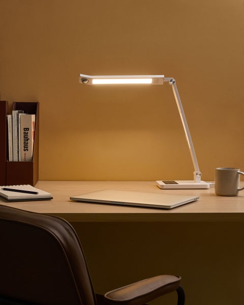Szene mit Schreibtischlampe, Laptop, Notizbuch und Tasse auf einem Schreibtisch.