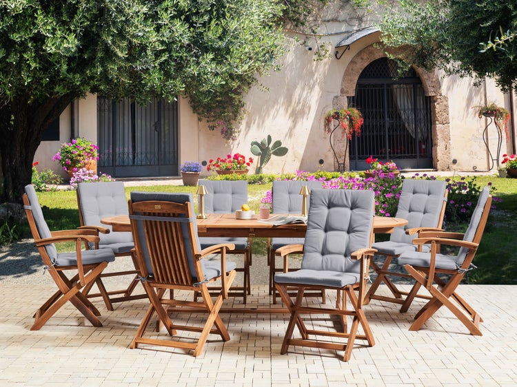 Gartenszene mit einem Holztisch und Stühlen mit grauen Kissen in einem Außenbereich.