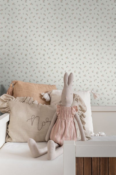 Helles Kinderzimmer mit Blumentapete. Ein weißes Holzbett ist mit strukturierten Stoffkissen und einem Stoffhasen in einem Kleid dekoriert.