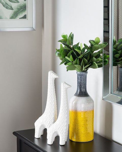 Dekoratives Stillleben mit Giraffenfiguren, Vase und Spiegel auf einem schwarzen Tisch.