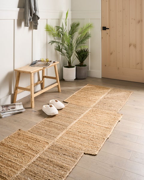 Ein hell gestalteter Flur mit einem Läufer aus Jute, einer Holzbank, Zimmerpflanzen und einer Holztür.