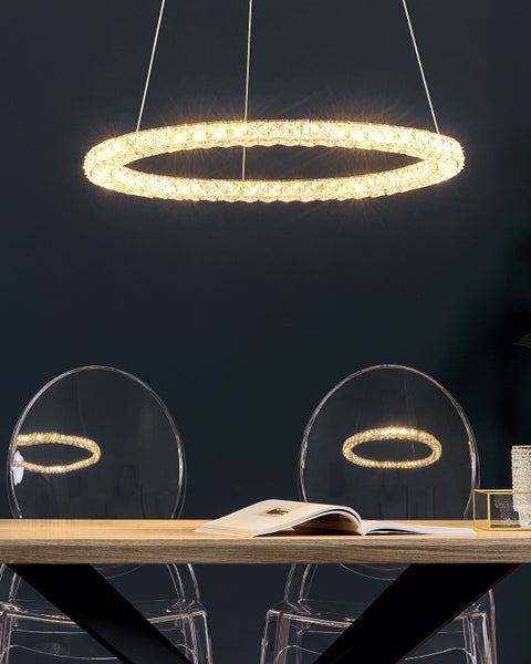 Ringförmige LED-Pendelleuchte aus Kristall über einem hölzernen Esstisch mit transparenten Stühlen.