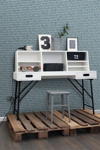 Dekoratives Arbeitszimmer mit Schreibtisch, Hocker und Holzpaletten als Bodenbelag vor einer gemusterten Tapete