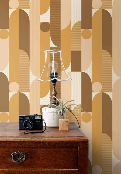 Retro-Tapete mit geometrischem Muster aus Kreisen und Streifen hinter einer Holzkommode mit Vintage-Kamera und Lampe.