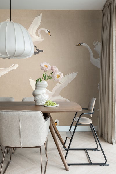 Esszimmer mit Holztisch, Stühlen, Blumenvase und Tapete mit Schwanenmotiven.