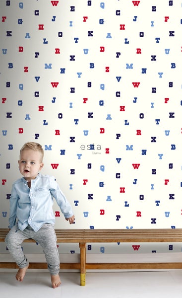 Kind sitzt vor einer Wandtapete mit Buchstabenmuster