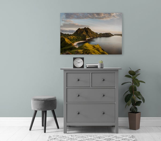 Wandbild mit einer Landschaftsaufnahme von Bergen und Meer über einer Kommode mit Hocker und Pflanze in einem modern eingerichteten Raum.