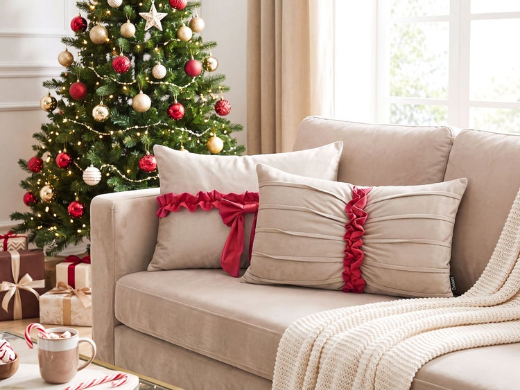 Zwei dekorative Zierkissen mit Rüschen in einer weihnachtlichen Wohnzimmerdekoration auf einem Sofa mit Weihnachtsbaum im Hintergrund.