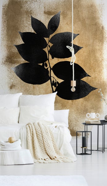Moderne Fototapete im Schlafzimmer mit schwarzem Blattmotiv auf strukturiertem, goldfarbenem Hintergrund.