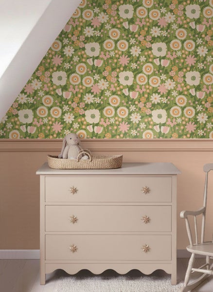 Helles Kinderzimmer mit Blumentapete über einer Wandvertäfelung, einer Kommode mit Sterngriffen und einem Stofftier in einem geflochtenen Korb.