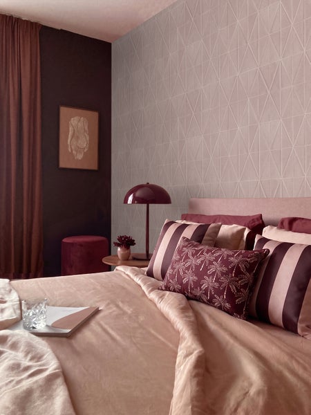 Modernes Schlafzimmer mit geometrisch gemusterter Tapete, passendem Bettzeug, gemusterten dekorativen Kissen und einer Tischleuchte.