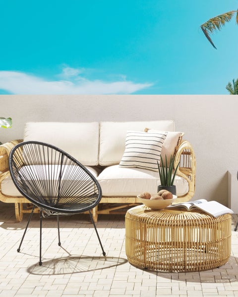 Szene mit Rattan-Sofa, schwarzem Stuhl und rundem Rattan-Tisch auf einer Terrasse