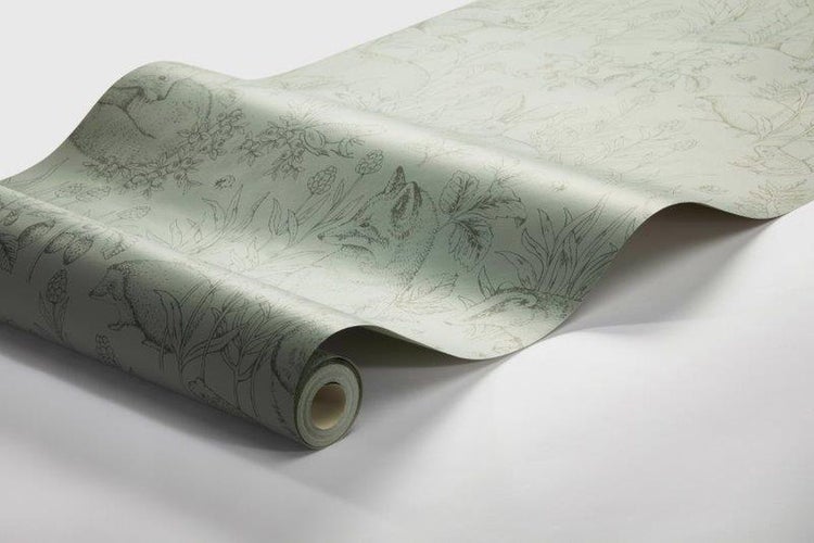 Dekorative Szene mit einer Tischlampe neben einem Bücherstapel auf einem Beistelltisch vor einer grünen Tapete mit Tiermotiven.