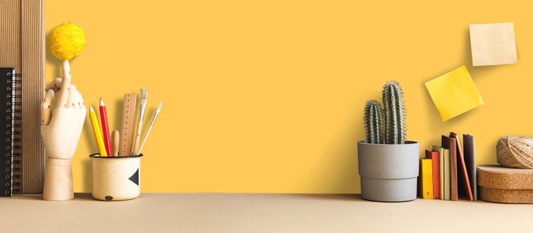 Strukturierter Arbeitsplatz mit Zeichenutensilien, Gliederhand aus Holz, Kaktus im Topf und Büchern vor einer hellen Wand.