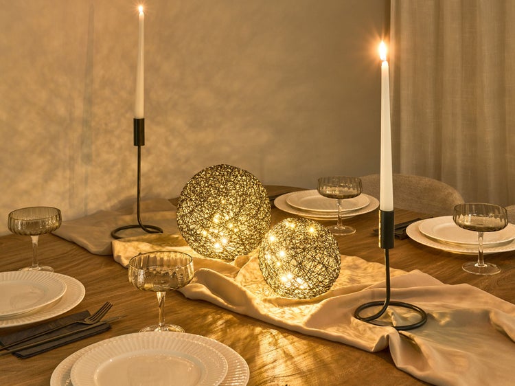 Dekorierter Esstisch mit Kerzen, LED-Kugeln, Geschirr und Gläsern für eine festliche Atmosphäre