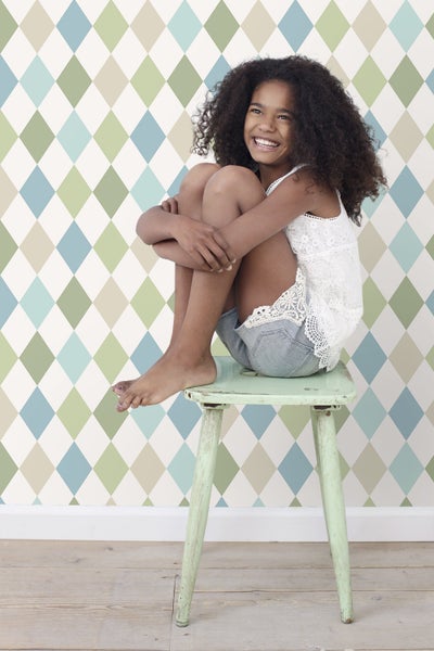 Mädchen sitzt auf einem Hocker vor einer Rauten Tapete