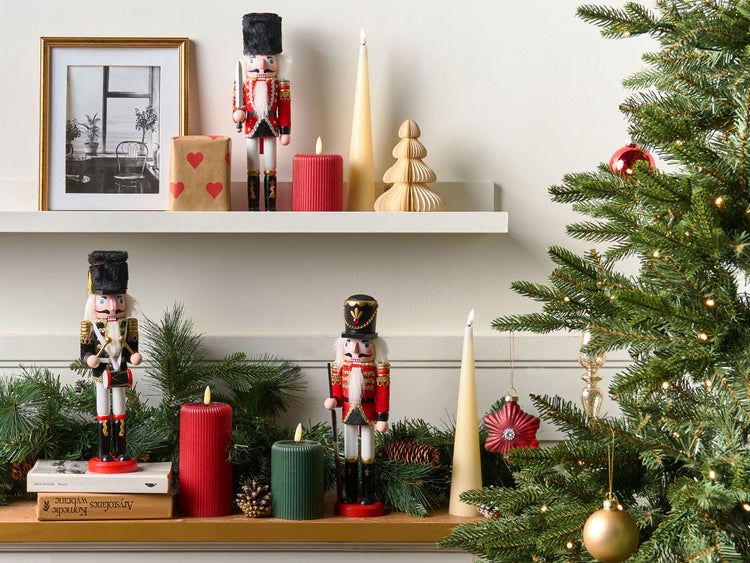 Festliche Dekoration mit Nussknackern, Kerzen und Weihnachtsbaum auf einem Regal.
