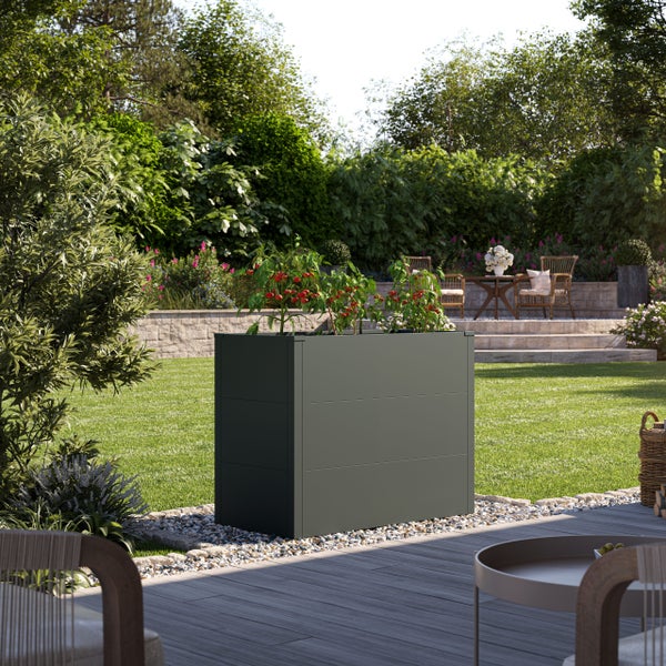 Modernes Metall-Hochbeet mit Tomatenpflanzen auf einer Kieselsteinfläche in einem hellen, gepflegten Garten mit Rasen und Terrasse.