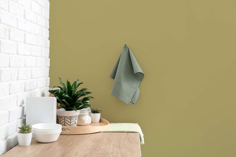 Organisierte Küchenszene mit olivgrüner Wand, weißer Ziegelwand, Holzplatte, Topfpflanzen und einem gestreiften Geschirrtuch.