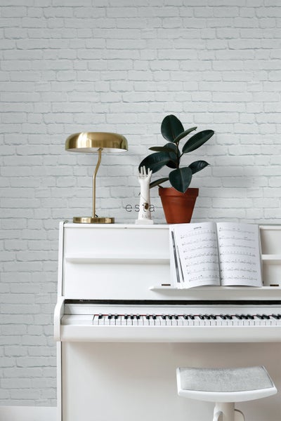 Szene mit weißem Klavier, Zimmerpflanze, goldener Lampe und Ziegelwandtapete