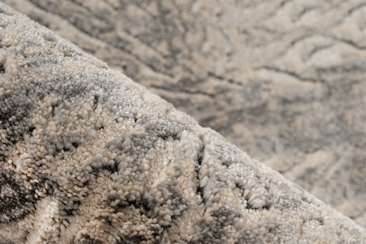Nahaufnahme eines grau-beigen Teppichs mit abstrakter Musterung und weichem Flor.